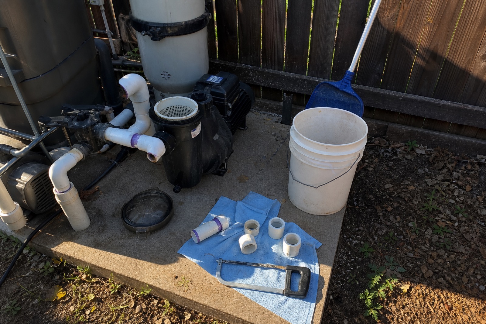 Mid-repair on a pool equipment pad with pump, PVC fittings, and skimmer parts laid out