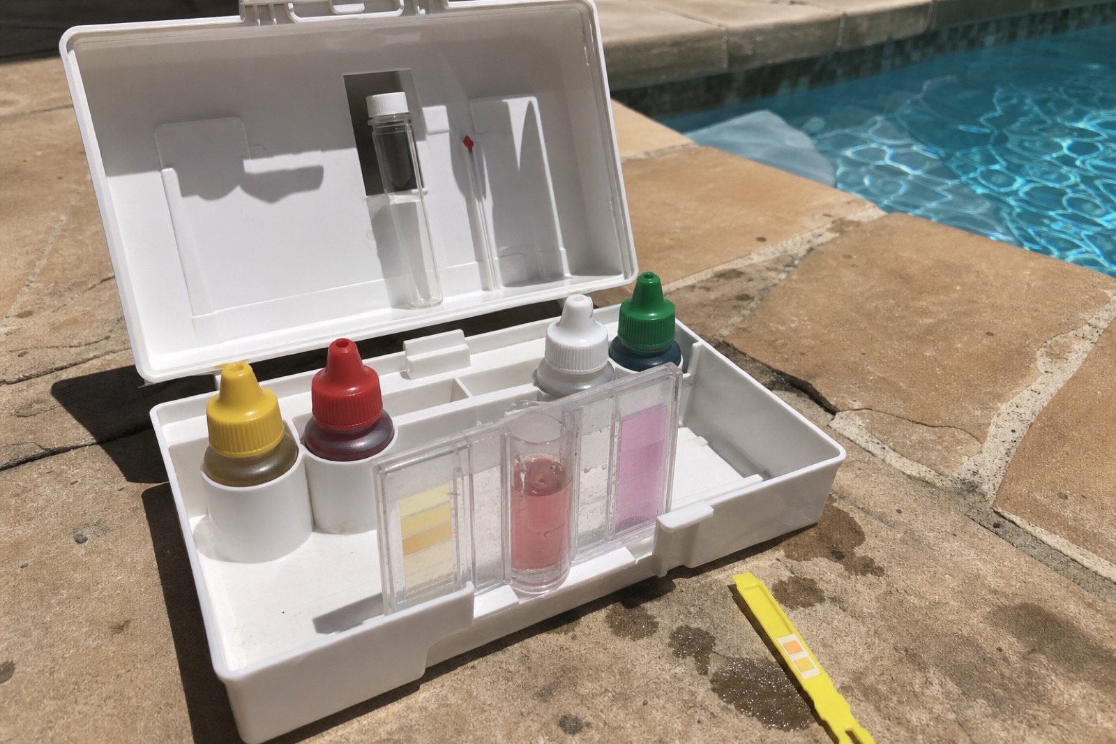 Open pool water test kit beside a pool deck
